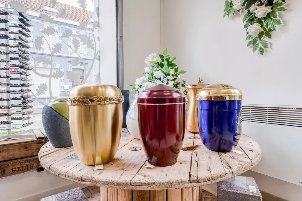 Urnes cinéraires de différentes couleurs exposées sur une table.